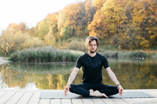 Jovem fazendo ioga asana na natureza perto do lago