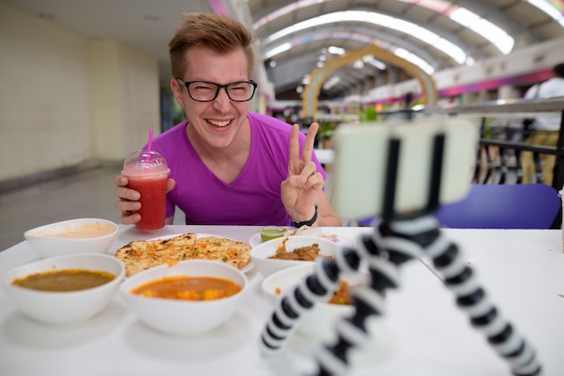 Jovem fazendo vlogs com celular em restaurante indiano