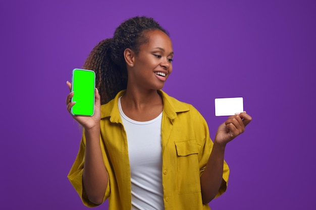 Jovem feliz afro-americana mostra telefone e cartão de crédito no estúdio