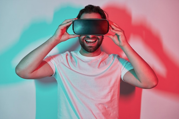 Jovem feliz ajustando seus óculos de realidade virtual com sombras coloridas no fundo