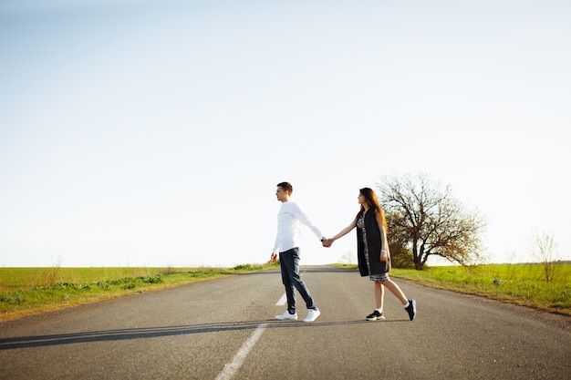 Jovem, feliz, amando o casal dançando na estrada de mãos dadas e olhando um ao outro