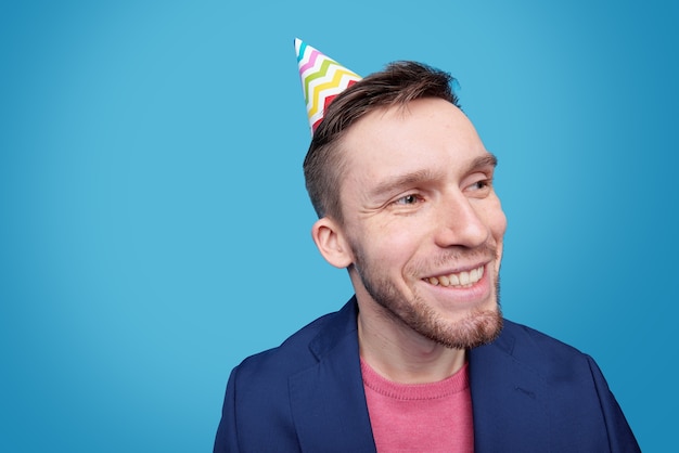 Jovem feliz com boné de aniversário na cabeça olhando para o lado com um sorriso cheio de dentes enquanto aproveita o evento festivo