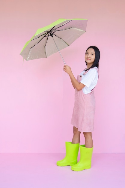 Jovem feliz com bota guarda-chuva verde verde sobre fundo rosa