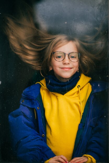 Jovem feliz com cabelo comprido e uma jaqueta quente atrás da janela