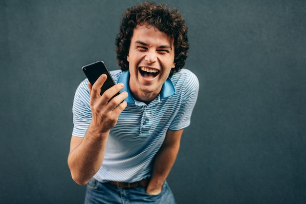 Jovem feliz com cabelo encaracolado falando no celular com sua namorada tem expressão alegre Macho alegre rindo durante uma chamada em seu telefone inteligente na rua da cidade Pessoas de estilo de vida