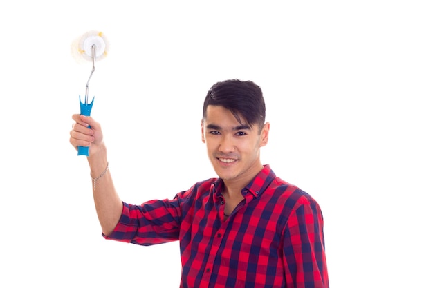 Jovem feliz com cabelo preto na camisa xadrez vermelha segurando rolo branco sobre fundo branco no estúdio