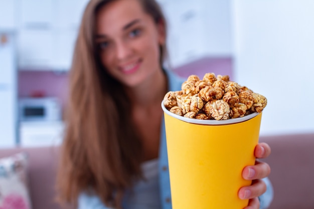 Jovem feliz com caixa de pipoca de caramelo crocante durante assistir filme em casa