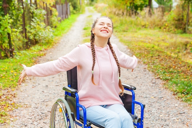 Jovem feliz com deficiência em cadeira de rodas na estrada no parque do hospital desfrutando de liberdade