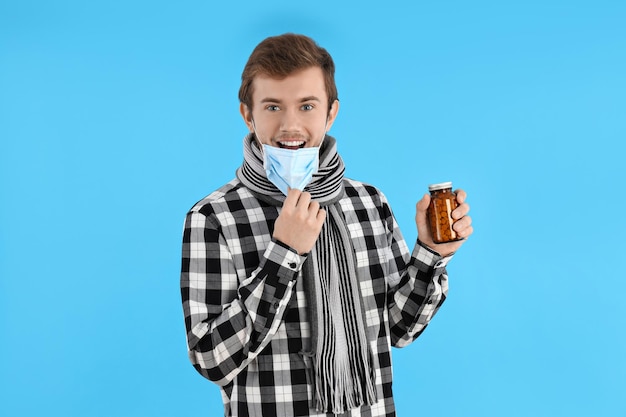 Jovem feliz com frio segura pílulas sobre fundo azul