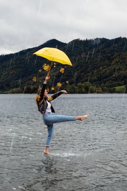 Jovem feliz com guarda-chuva amarelo no outono no foco seletivo da chuva