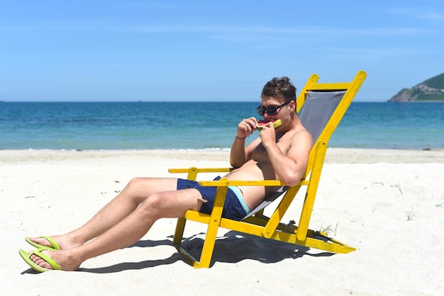 Jovem feliz comendo melancia sentado na espreguiçadeira em uma praia do sul da china no Vietnã