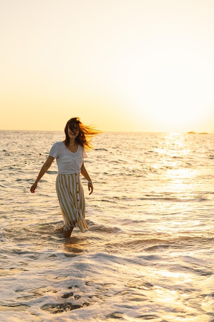 Jovem feliz dançando girando pelo mar em um vestido amarelo esvoaçante