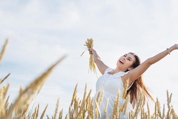 Jovem feliz de vestido branco em pé em um campo de trigo com o nascer do sol ao fundo