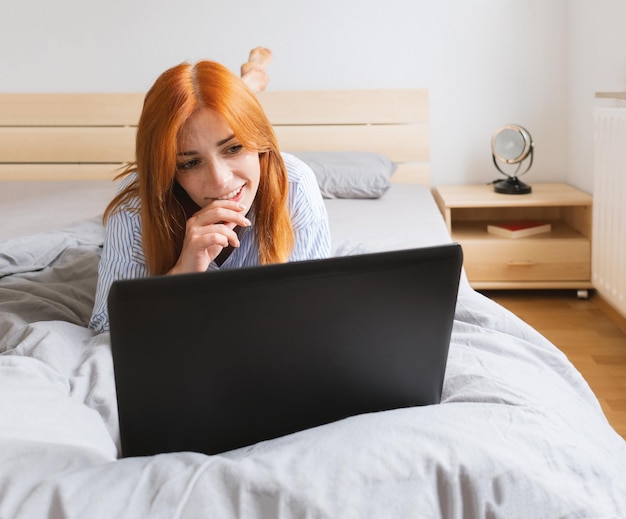 jovem feliz deitada com um laptop na cama