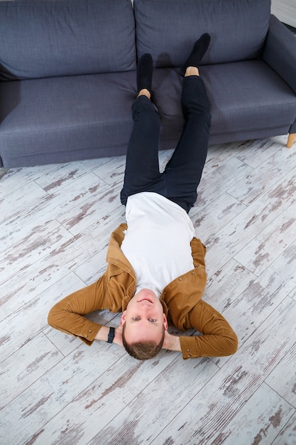 Jovem feliz deitado no chão perto do sofá da sala e descansando