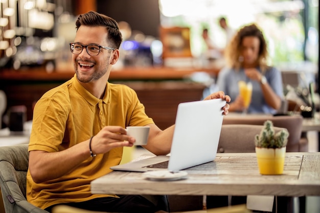 Jovem feliz desfrutando de uma xícara de café enquanto usa o computador e relaxa em um café