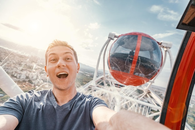 Jovem feliz e animado tirando foto de selfie na cabine de uma roda gigante Aventuras de viagem solo e diversões ou luna park