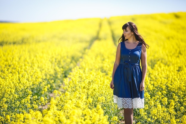 Jovem feliz e linda modelo de tamanho grande de vestido azul no campo de colza florescente no verão