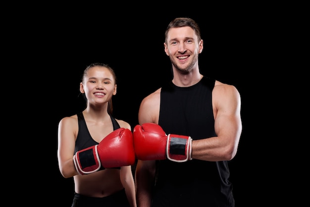 Jovem feliz e mulher em trajes esportivos olhando para você com sorrisos enquanto se tocam com as mãos em luvas de boxe