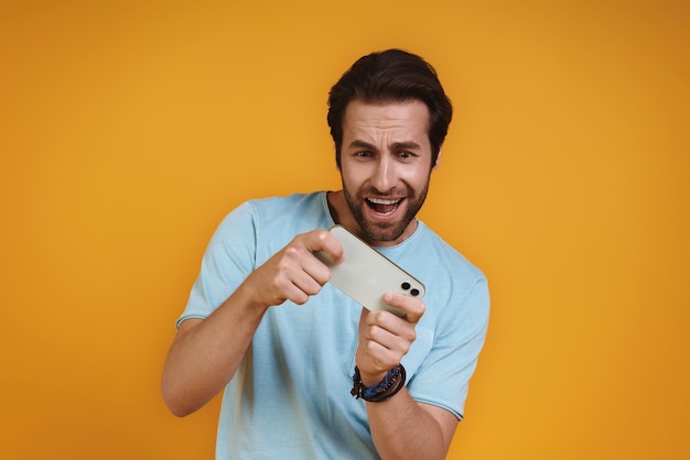 Jovem feliz em roupas casuais, jogando no telefone inteligente e sorrindo