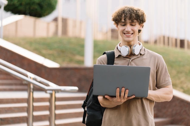 Jovem feliz estudante universitário ou universitário com mochila e fones de ouvido usando laptop