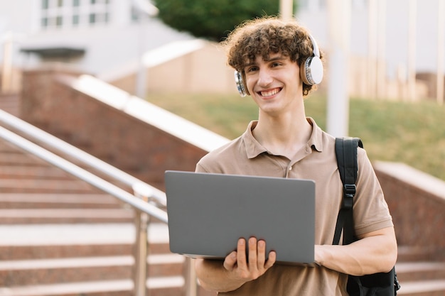 Jovem feliz estudante universitário ou universitário com mochila e fones de ouvido usando laptop