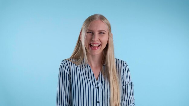 Jovem feliz explodindo de rir sobre fundo azul. Ela tem um longo cabelo loiro.