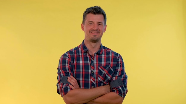 Jovem feliz explodindo em gargalhadas sobre fundo amarelo, ele está com uma camisa quadriculada k