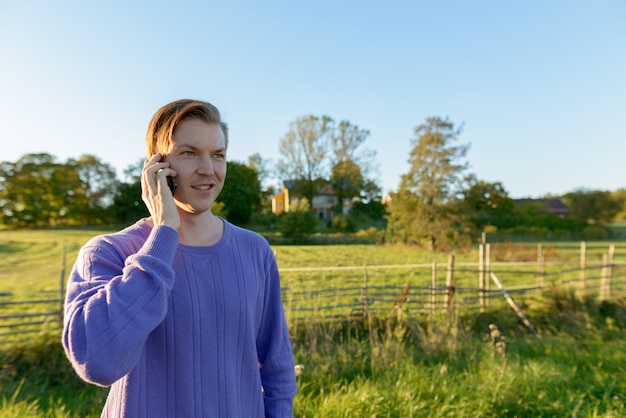 Jovem feliz falando no celular em uma planície pacífica e gramada com a natureza