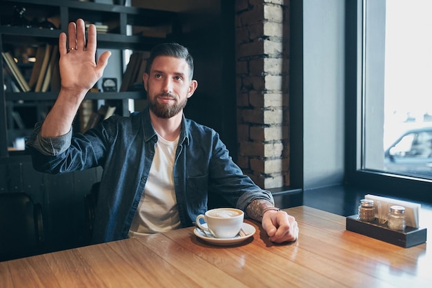Foto jovem feliz homem barbudo bebendo café fresco da manhã. caucasiano bonito homem profissional de negócios tomando café dentro de casa. diga olá