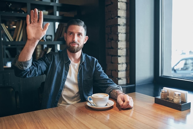 Jovem feliz homem barbudo bebendo café fresco da manhã. Caucasiano bonito homem profissional de negócios tomando café dentro de casa. Diga olá