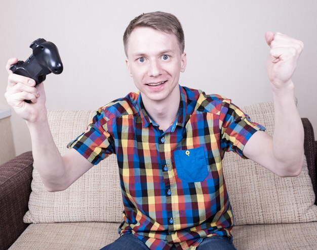 Jovem feliz jogando videogame sentado no sofá e segurando o controle remoto