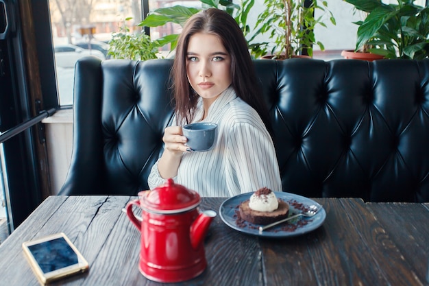 jovem feliz lendo em seu telefone celular enquanto está sentada no interior de uma cafeteria moderna