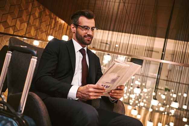 Jovem feliz lendo jornal enquanto está sentado no restaurante do hotel