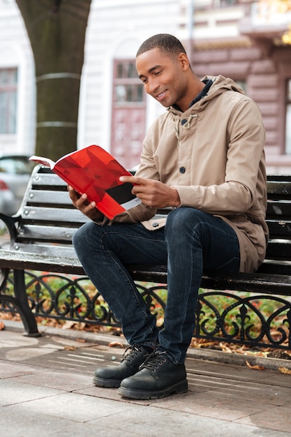 Jovem feliz lendo um livro enquanto está sentado no banco da rua