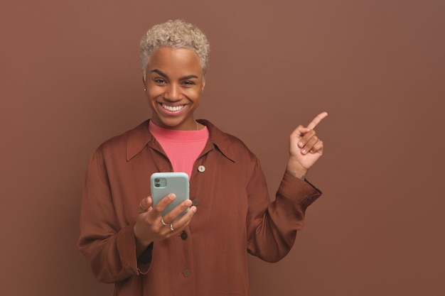 Jovem feliz linda mulher afro-americana com telefone aponta o dedo para o lado