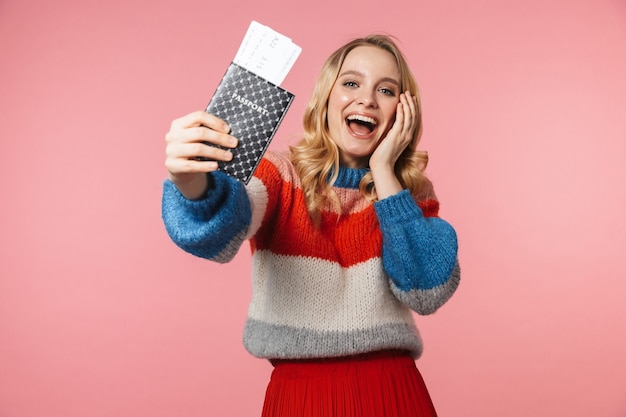 jovem feliz linda mulher posando isolada na parede rosa segurando passaporte com ingressos