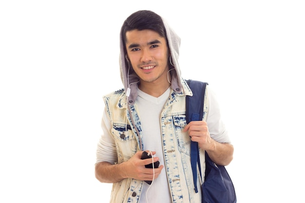 Jovem feliz na jaqueta jeans com mochila azul usando smartphone e fones de ouvido