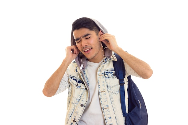 Jovem feliz na jaqueta jeans com mochila azul usando smartphone e fones de ouvido