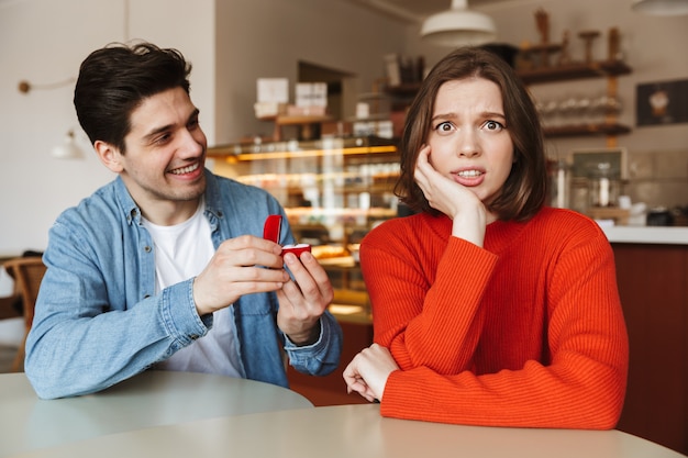 Jovem feliz pedindo casamento a uma mulher confusa