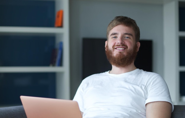 Jovem feliz positivo usa computador portátil em casa na sala de estar sentado no sofá olhando para a câmera