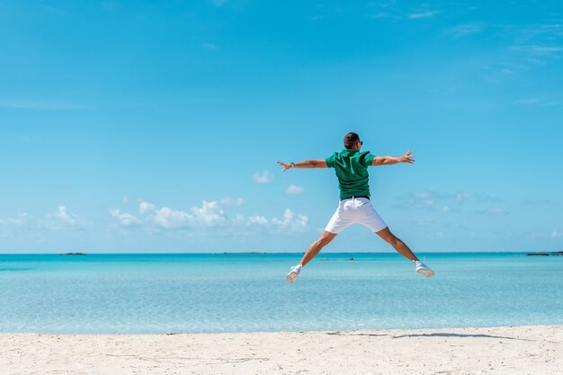 Jovem feliz pulando com os braços estendidos na praia