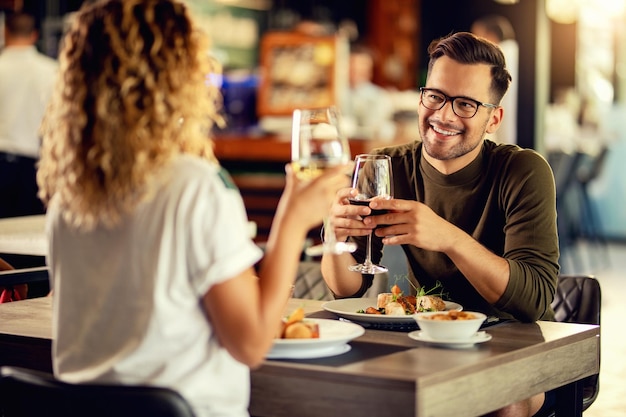 Jovem feliz se comunicando com sua namorada enquanto almoça e bebe vinho em um restaurante