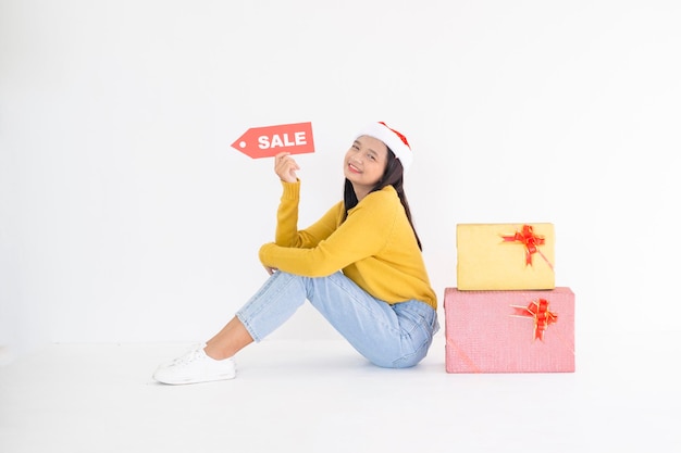 Jovem feliz segura caixa de presente, menina asiática usa suéter amarelo sobre fundo branco.