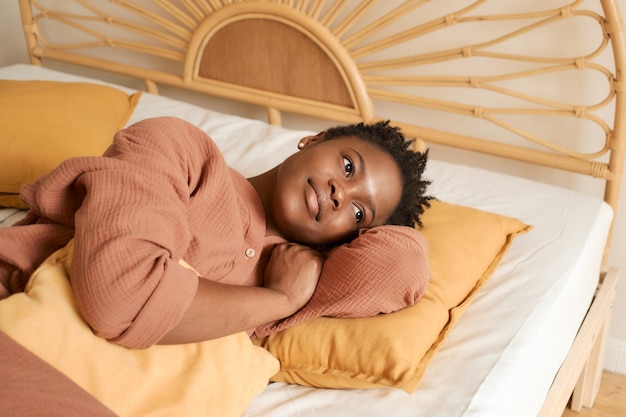 Jovem feliz sentada na cama do quarto, usando um pijama de musselina no laptop, conversando com os amigos