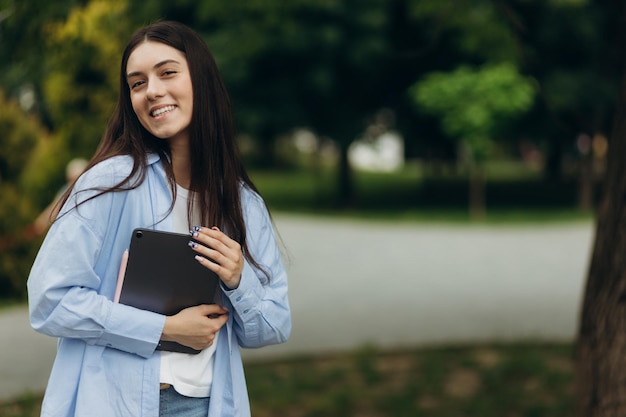 Jovem feliz sorridente jovem estudante de negócios caucasiana andando conceito no parque verde de verão ao ar livre segurando tablet Espaço para cópia