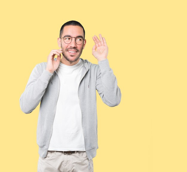 Jovem feliz sorrindo e fazendo um gesto de tentar ouvir algo