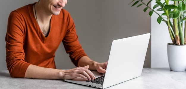 Jovem feliz, sorrindo, enquanto trabalha em seu laptop.