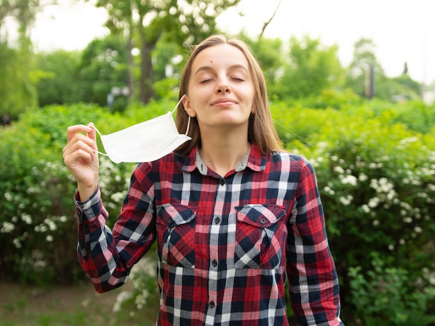 Jovem feliz tira uma máscara médica e respira ar fresco na natureza