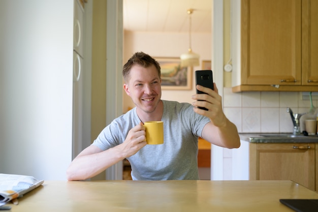 Jovem feliz tirando uma selfie enquanto bebe café na janela